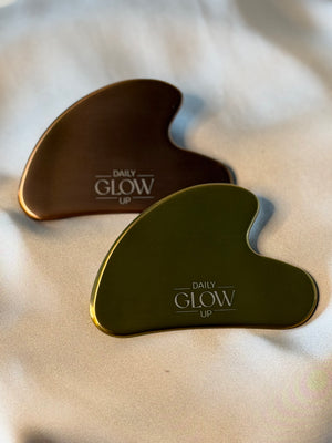 Gua Sha Stein in Gold, dahinter Gua Sha Stein in Bronze auf Seidenstoff
