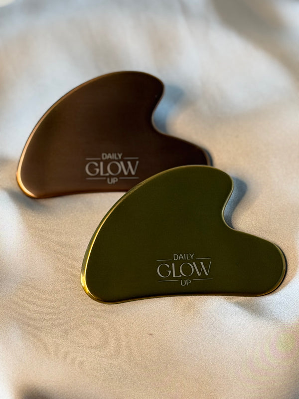 Gua Sha Stein in Gold, dahinter Gua Sha Stein in Bronze auf Seidenstoff