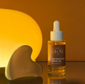 Daily Glow Up Facial Oil und Gua Sha Stein in einer warmen glowigen Pflegeszene.