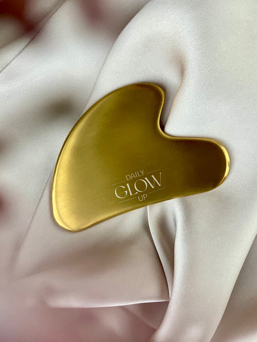 Goldener Gua Sha Stein von Daily Glow Up für eine entspannende Gesichtsmassage.