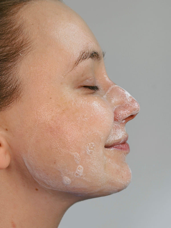Frau mit Reinigungsschaum im Gesicht bei der Anwendung des Daily Glow Up Hydra-Glow Reinigungsgels.
