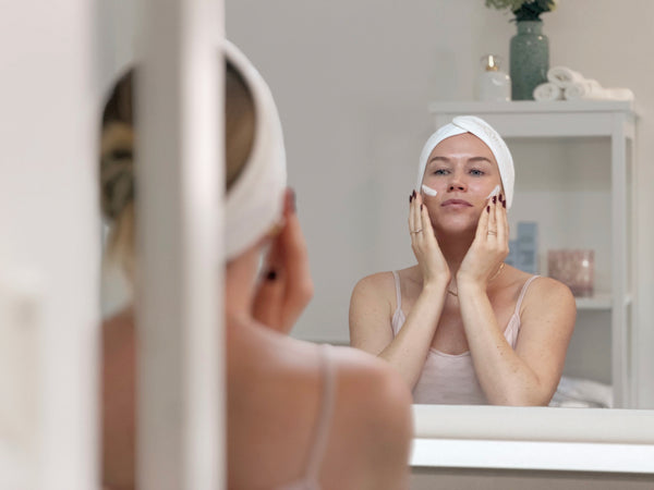 Frau trägt die Daily Glow Up Multi-Hyaluron Tagescreme vor dem Spiegel auf.