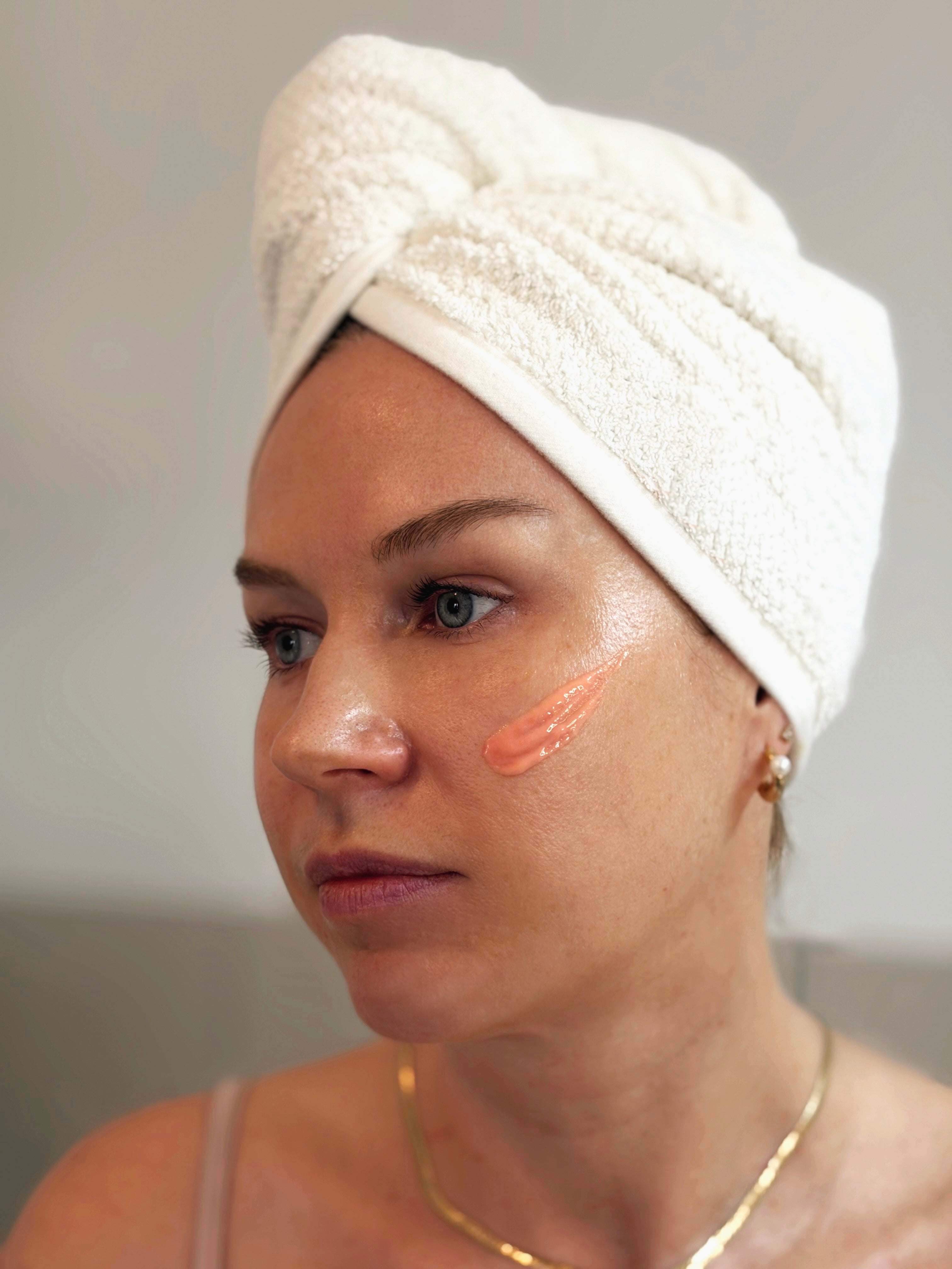 Frau mit Daily Glow Up Peptid Serum auf der Wange während der Gesichtspflege.