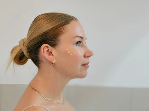Frau mit Daily Glow Up Vitamin C Serum auf der Wange während der Pflegeroutine.